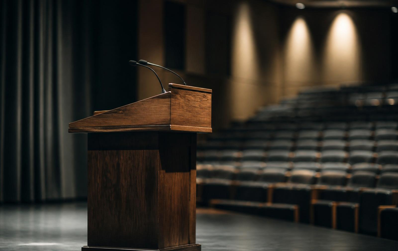 Empty wooden lecture podium on a softly lit stage