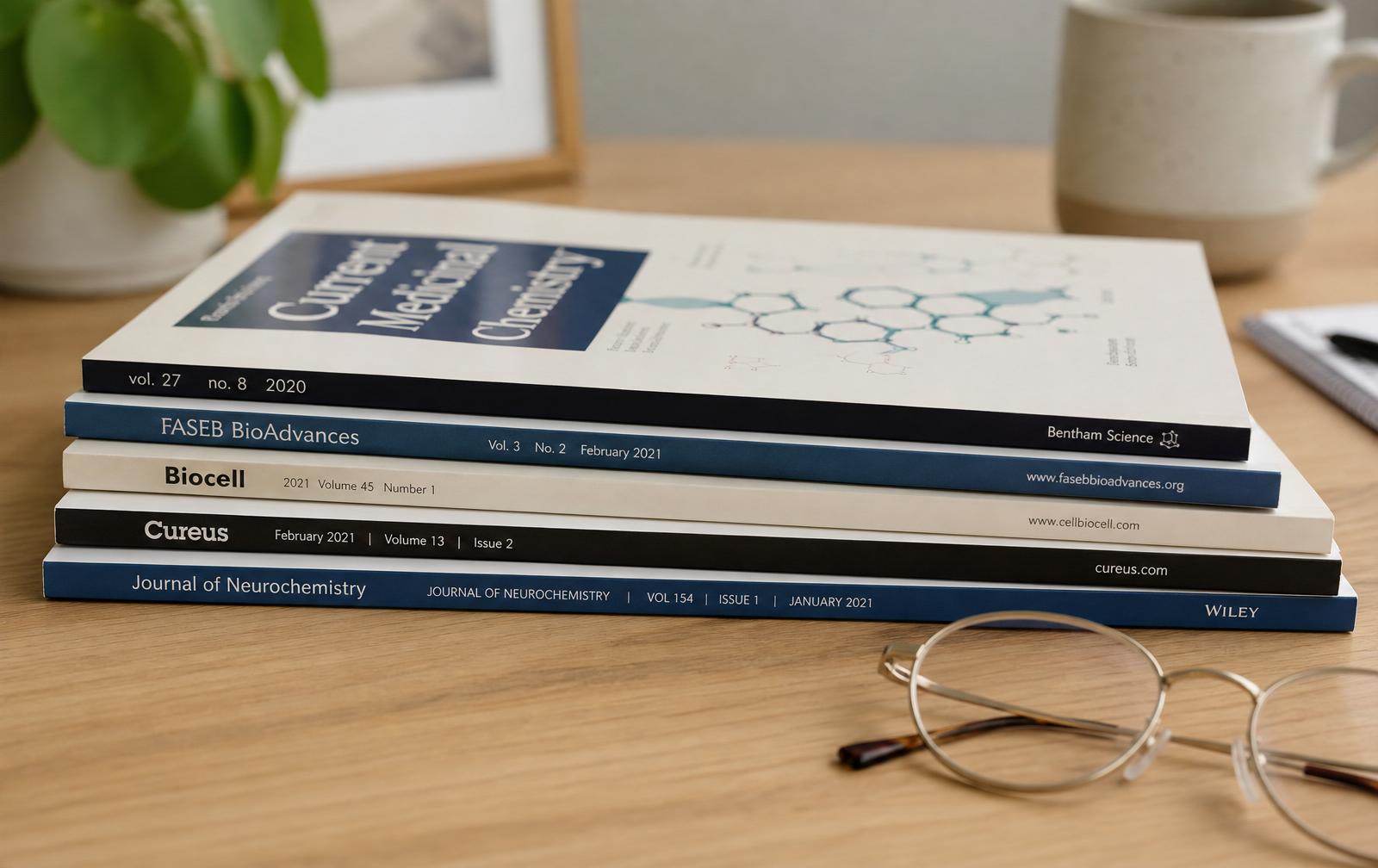 Stack of medical journals with reading glasses resting on top in warm window light